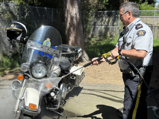 Corporal Peter Somerville pressure washing his RCMP motorcycle in a parking lot