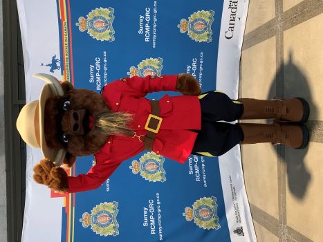 A bison mascot dressed in formal RCMP red serge, wearing a red serge jacket, brown boots and brown Stetson hat raising one hand in a salute.